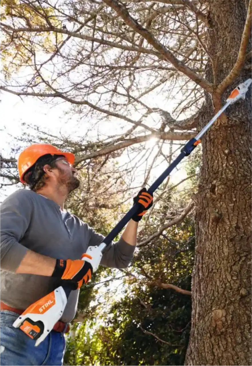 Operador com capacete usando motopoda Stihl para podar galhos altos de uma árvore