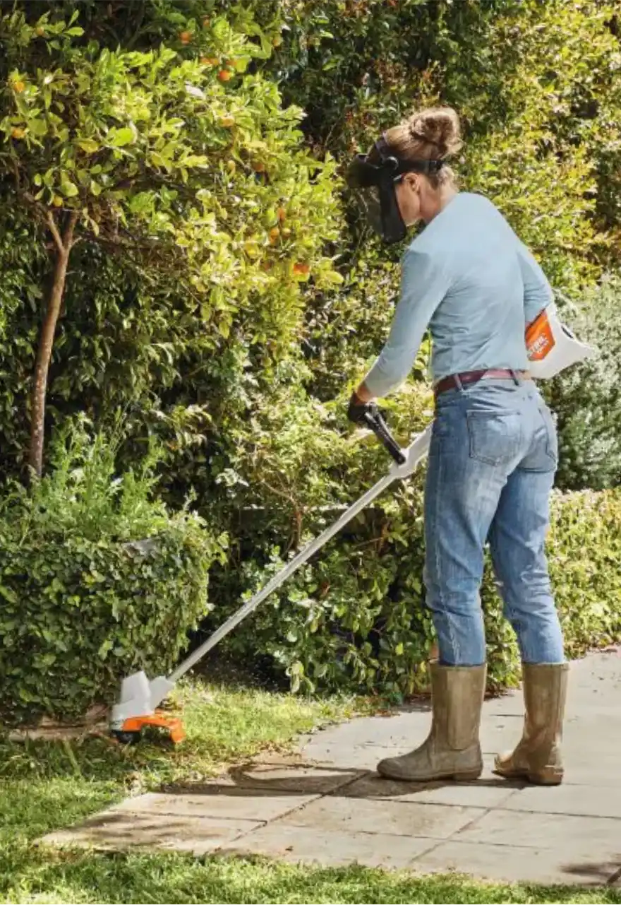 Jardineira usando roçadeira para aparar a grama ao lado de uma calçada
